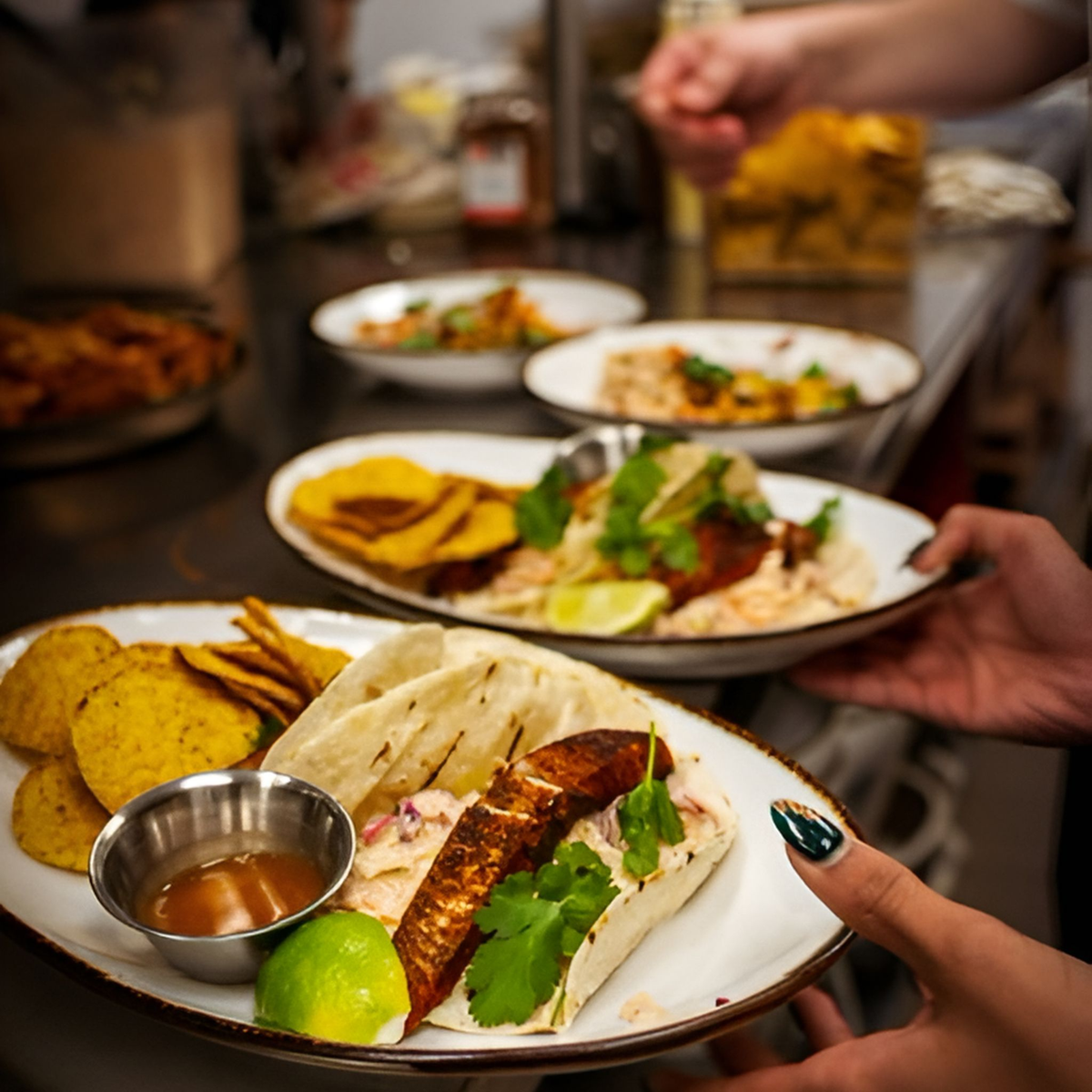 Shared table of tacos and plantain chips served with Liquid Gold mango hot sauce