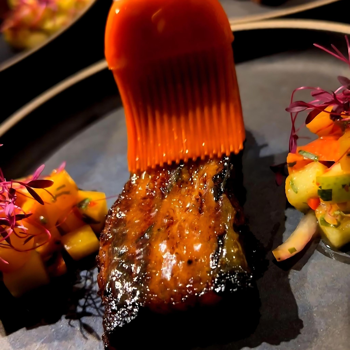 Basting pork belly with La Jefa garlic scorpion hot sauce next to mango salsa