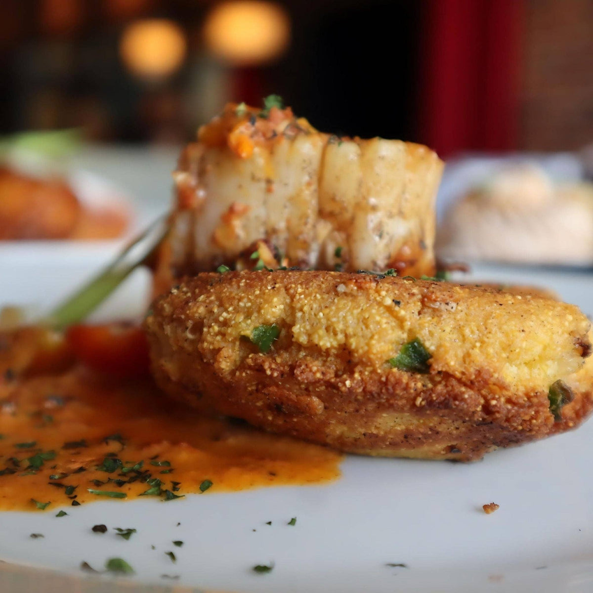 Crab cake plated on a fried green tomato with a La Jefa garlic scorpion hot sauce drizzle