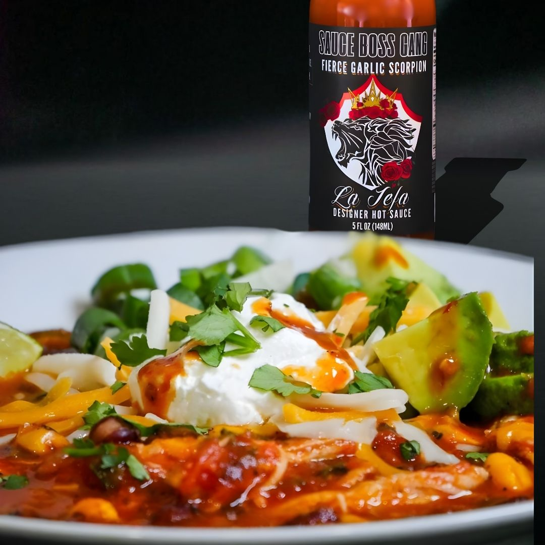 La Jefa hot sauce bottle behind a bowl of chicken tortilla soup with avocado and crema