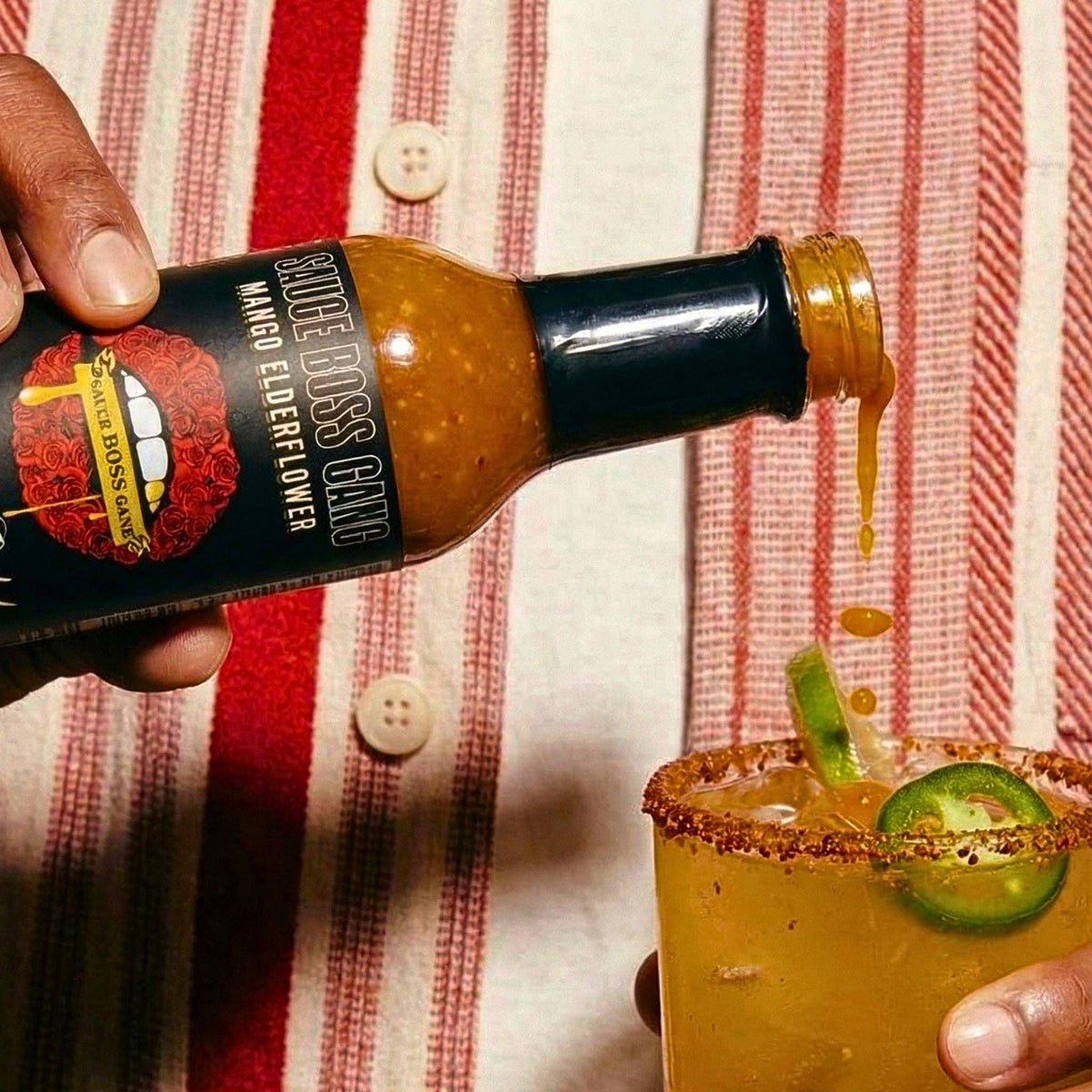 Pouring Liquid Gold mango scotch bonnet hot sauce into a chili-rimmed mango margarita